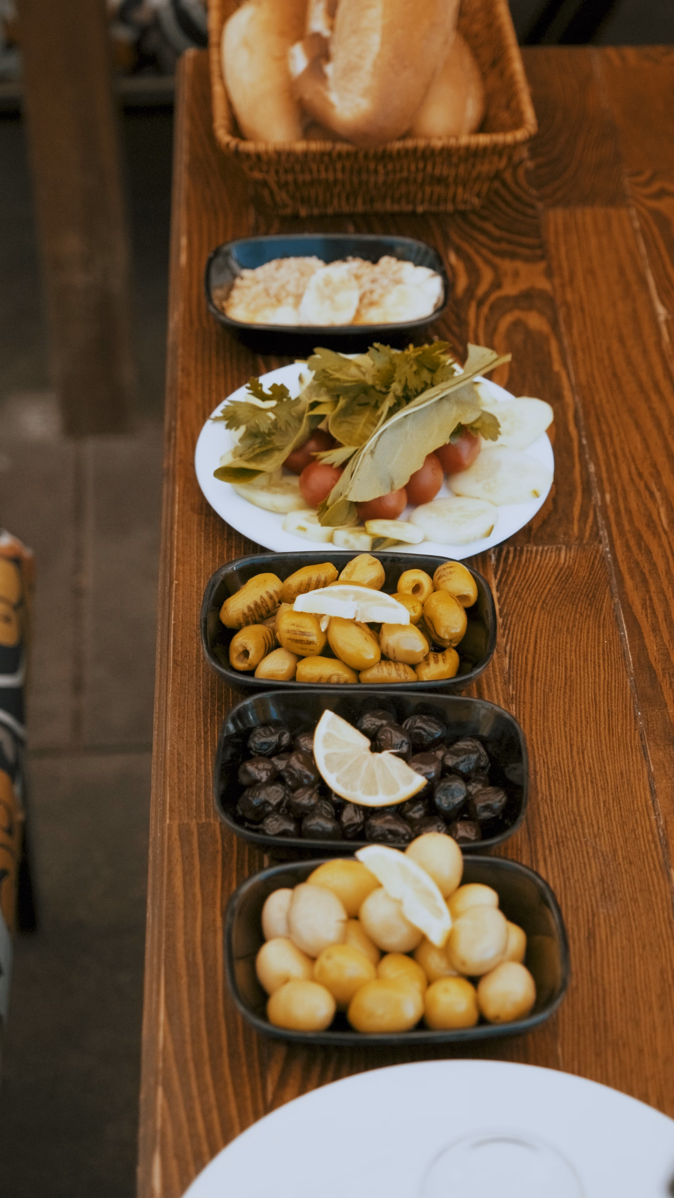 Ahşap masada sıralanmış zeytinler, turşu, salata ve ekmek sepeti
